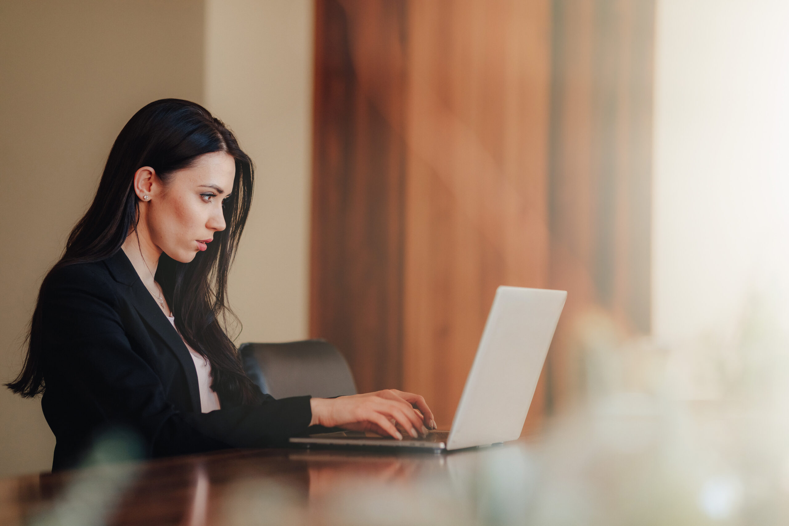 Young attractive emotional girl in business-style clothes sitting at a desk on a laptop and phone in the office or auditorium